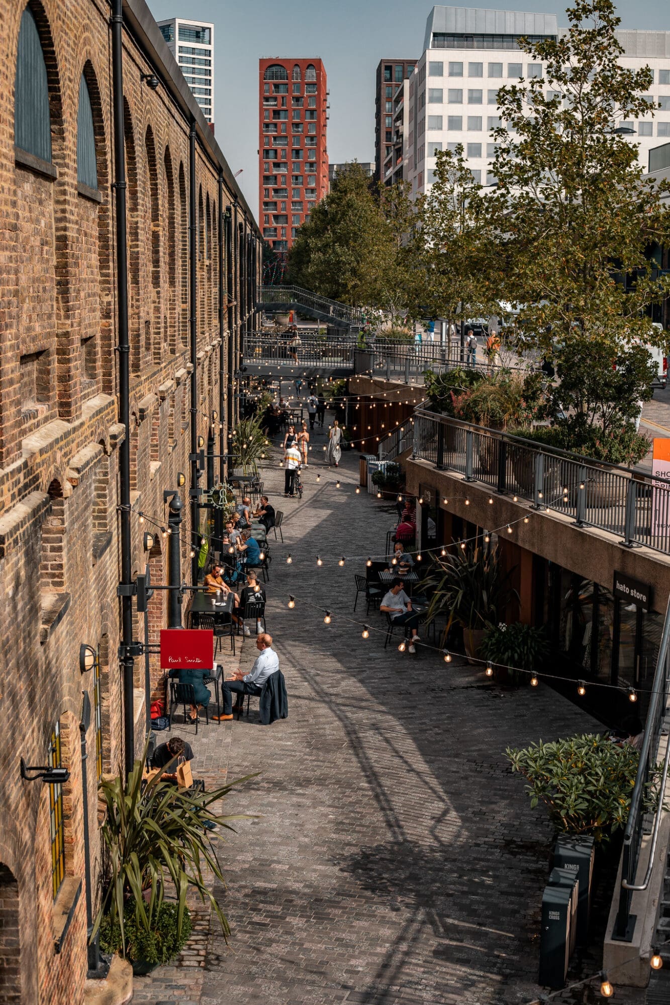 A narrow alley in Coal Drops Yard, where people sit and eat and browse the shops under a canopy of festoon lights.