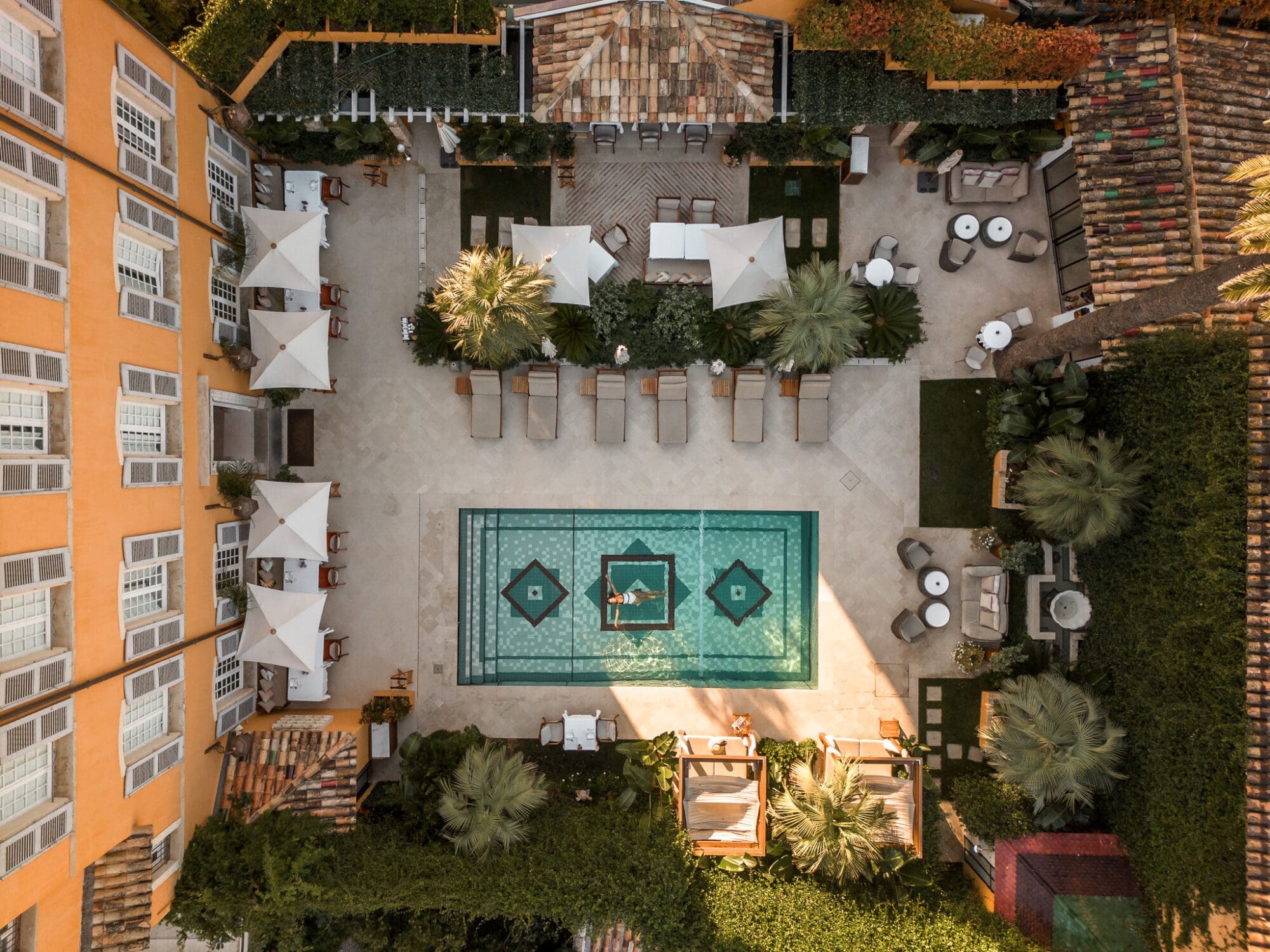 An aerial drone shot of the courtyard at Airelles Pan Deï Palace in Saint Tropez, with Anoushka floating in the rectangular square pool.