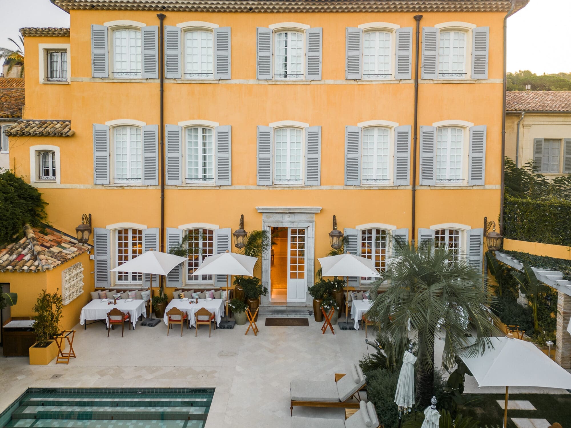The exterior of Airelles Pan Deï Palais Saint Tropez, a yellow building with shuttered windows and a turquoise pool in the foreground.